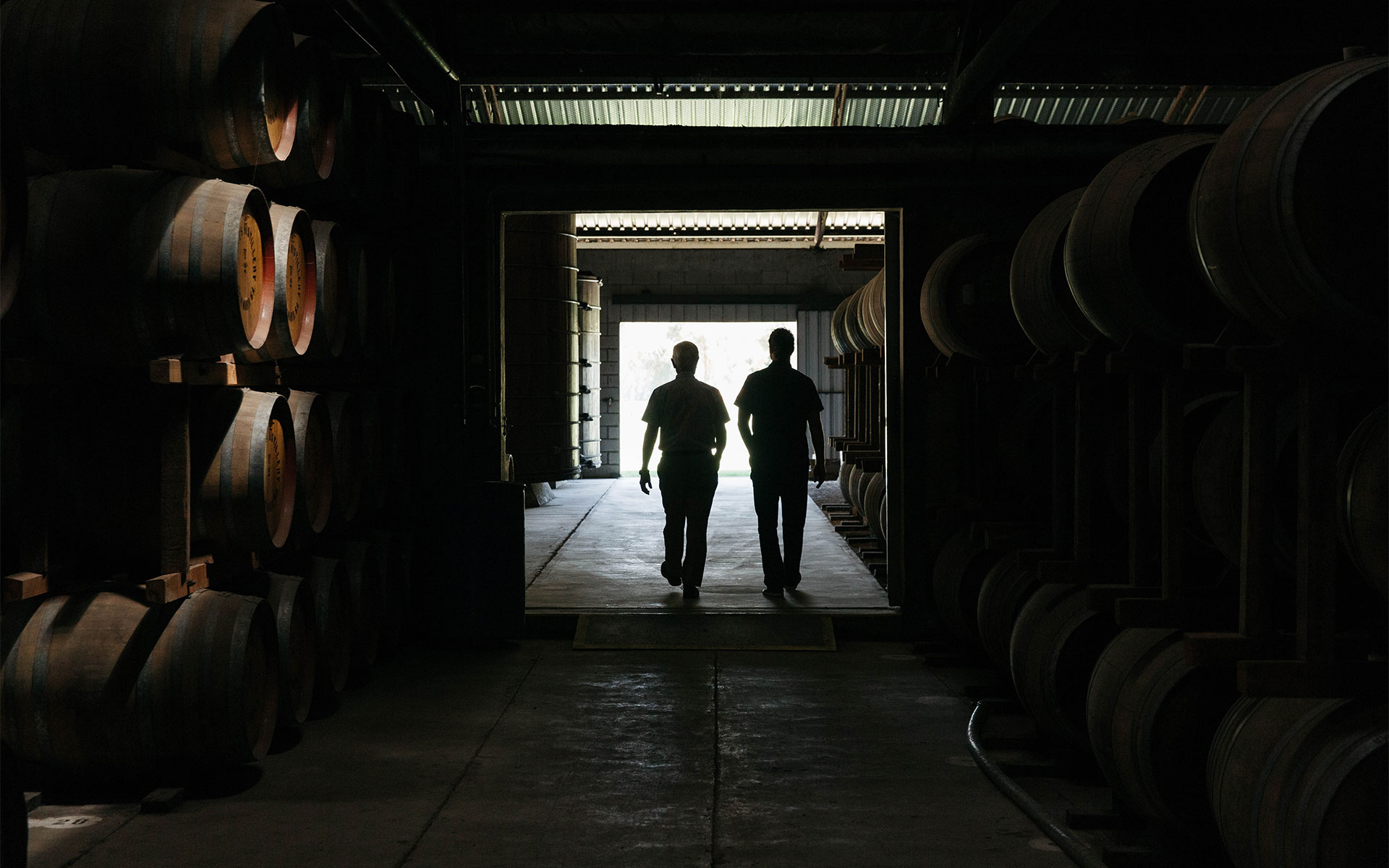 Two staff members silhouetted against an open doorway, existing the St Agnes Distillery barrel cellar